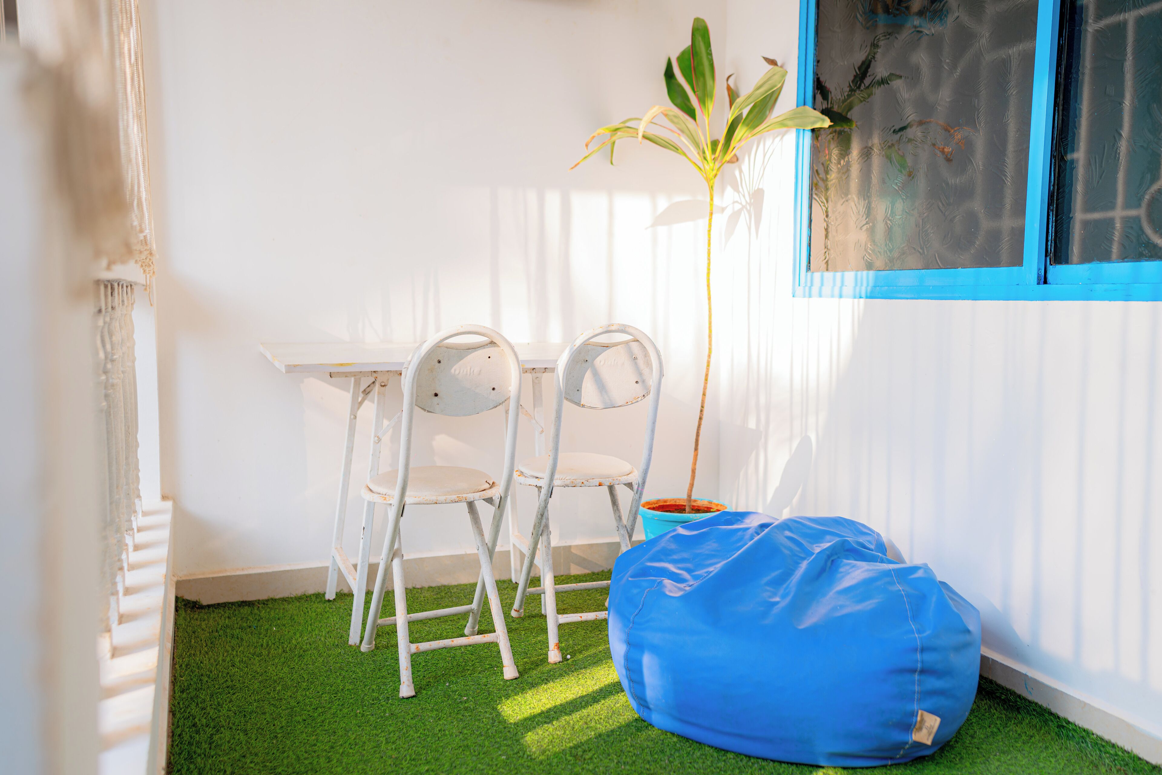 A room with a small table and two chairs, a blue bean bag, and a potted plant.