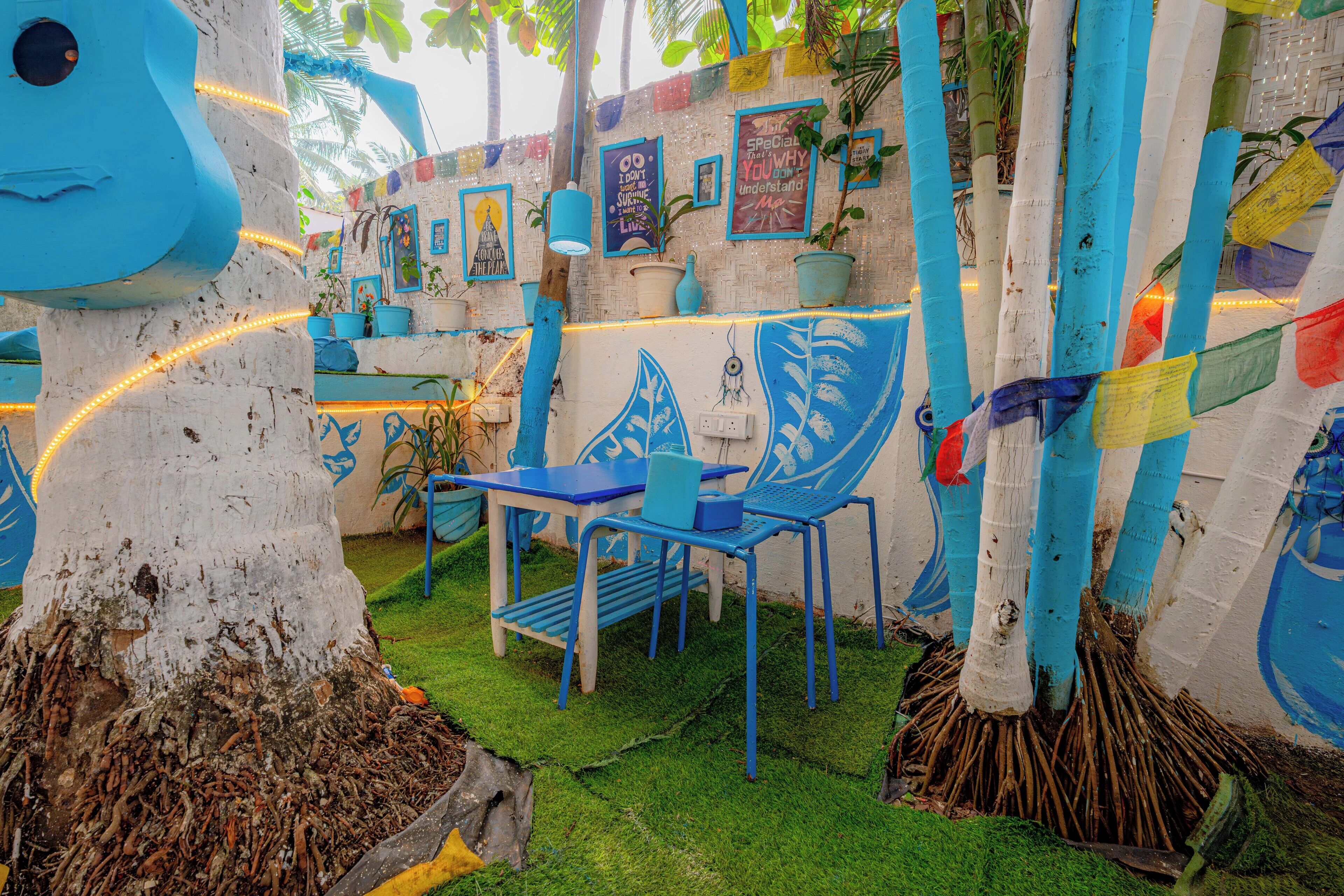 A vibrant outdoor seating area with blue chairs and tables, surrounded by bamboo poles and potted plants.