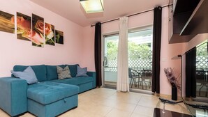 Ein modernes Wohnzimmer mit einem petrolfarbenen Sofa, einem Glastisch und einer Schiebetür zu einer Außenpatio.