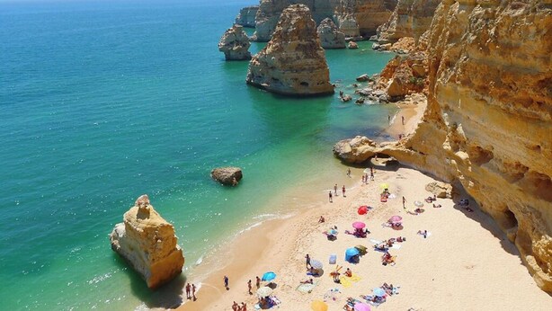 Ein Strand mit klarem türkisfarbenem Wasser, Felsformationen und Menschen, die sich sonnen.