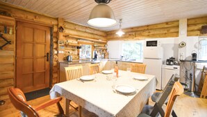 A wooden cabin interior with a dining area, kitchen, and a large wooden door.