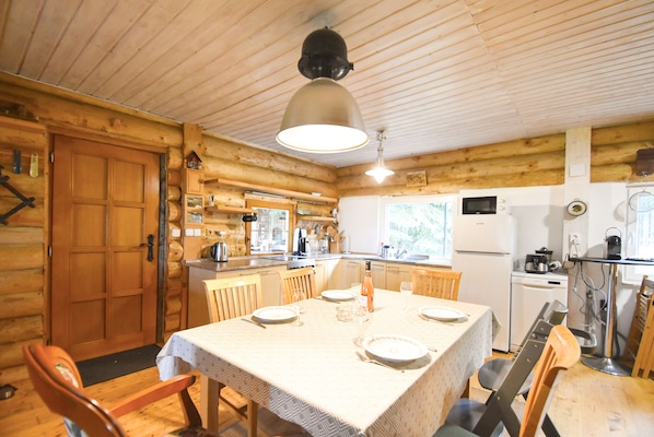 Interno di una baita in legno con zona pranzo, cucina e un'ampia porta di legno.