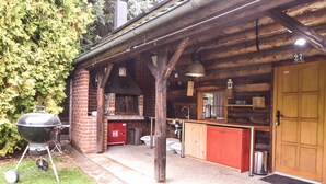 A rustic cabin with a brick exterior, a wooden porch, a red kitchen, and a black grill.
