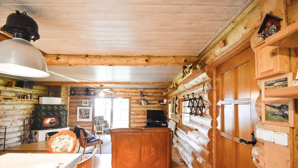 A log cabin interior with a wooden dining table, chairs, a sofa, a fireplace, and a television.