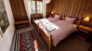A wooden-paneled bedroom with a large bed, bedside lamps, a bench, and a window with curtains. - MAGNIFICENT VIEWS FROM THE HEART OF VERBIER-NEXT TO THE NEW SPORTS CENTER (Val de Bagnes)