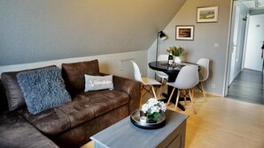 Ein modernes Wohnzimmer mit einem braunen Sofa, einem Couchtisch mit einer Pflanze und einem Essbereich mit Tisch und Stühlen.