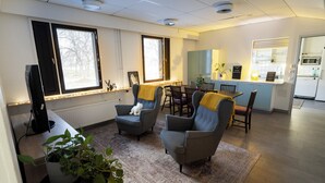 Una sala moderna con dos sillones, una mesa de centro y un comedor con mesa y sillas. Se ve una cocina al fondo.