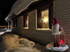 A snow-covered house with a star decoration in the window and a Santa Claus figure outside.