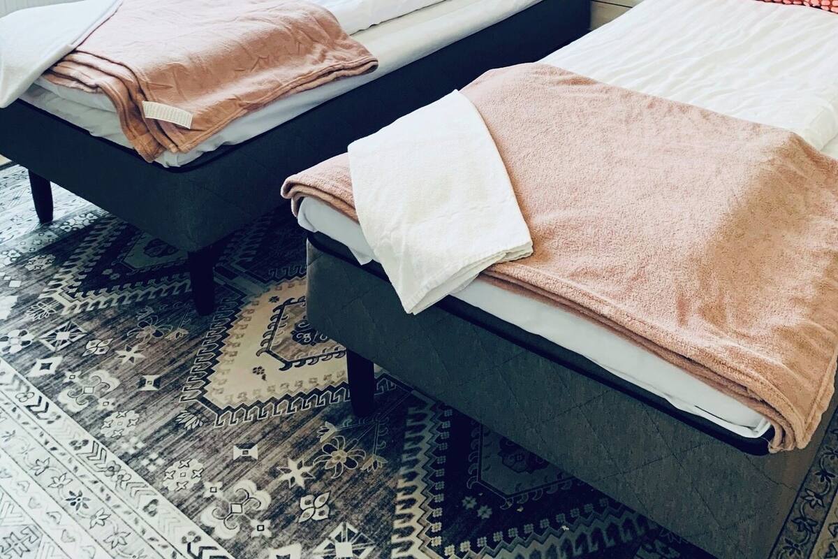 A hotel room with two beds, a window with curtains, a patterned rug, and three framed pictures on the wall.