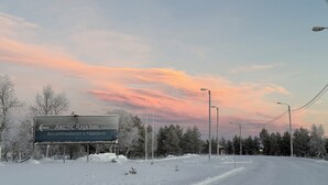 Señal del Arctic Raja Inn con una flecha direccional, rodeado de árboles cubiertos de nieve y un cielo al atardecer.