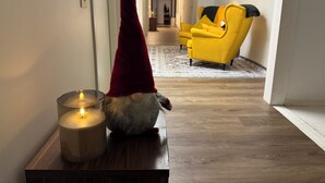 Una figurita de gnomo con sombrero rojo y una vela encendida sobre una mesa de madera en un pasillo.