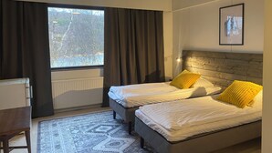 Habitación de hotel con dos camas, un escritorio y una ventana con cortinas.