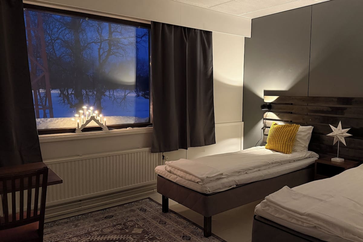 A bedroom with two beds, a nightstand, a chair, and a window with curtains.