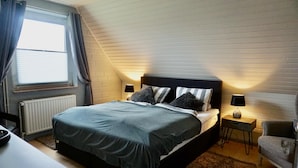 Une chambre à coucher avec un lit, des tables de chevet, une chaise, un radiateur et une fenêtre avec des rideaux.
