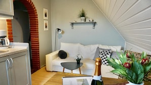 Un salon moderne avec un canapé blanc, une petite table basse, un vase rempli de fleurs et une bouteille de champagne.