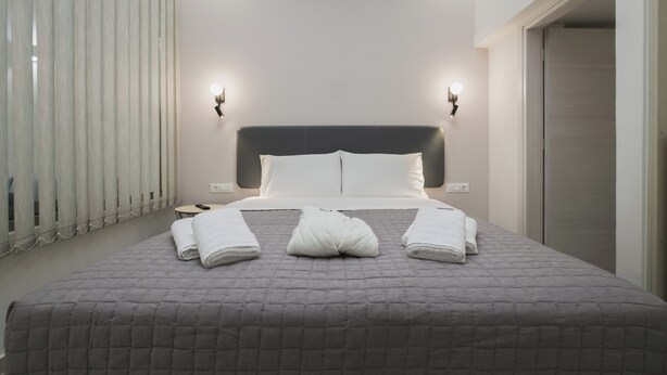 Quarto de hotel moderno com uma cama grande, duas mesas de cabeceira e um criado-mudo.