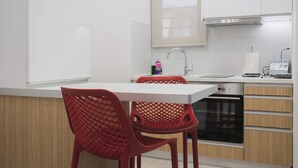 Cozinha moderna com armários brancos, coifa de aço inoxidável, forno embutido e uma cadeira de plástico vermelha.