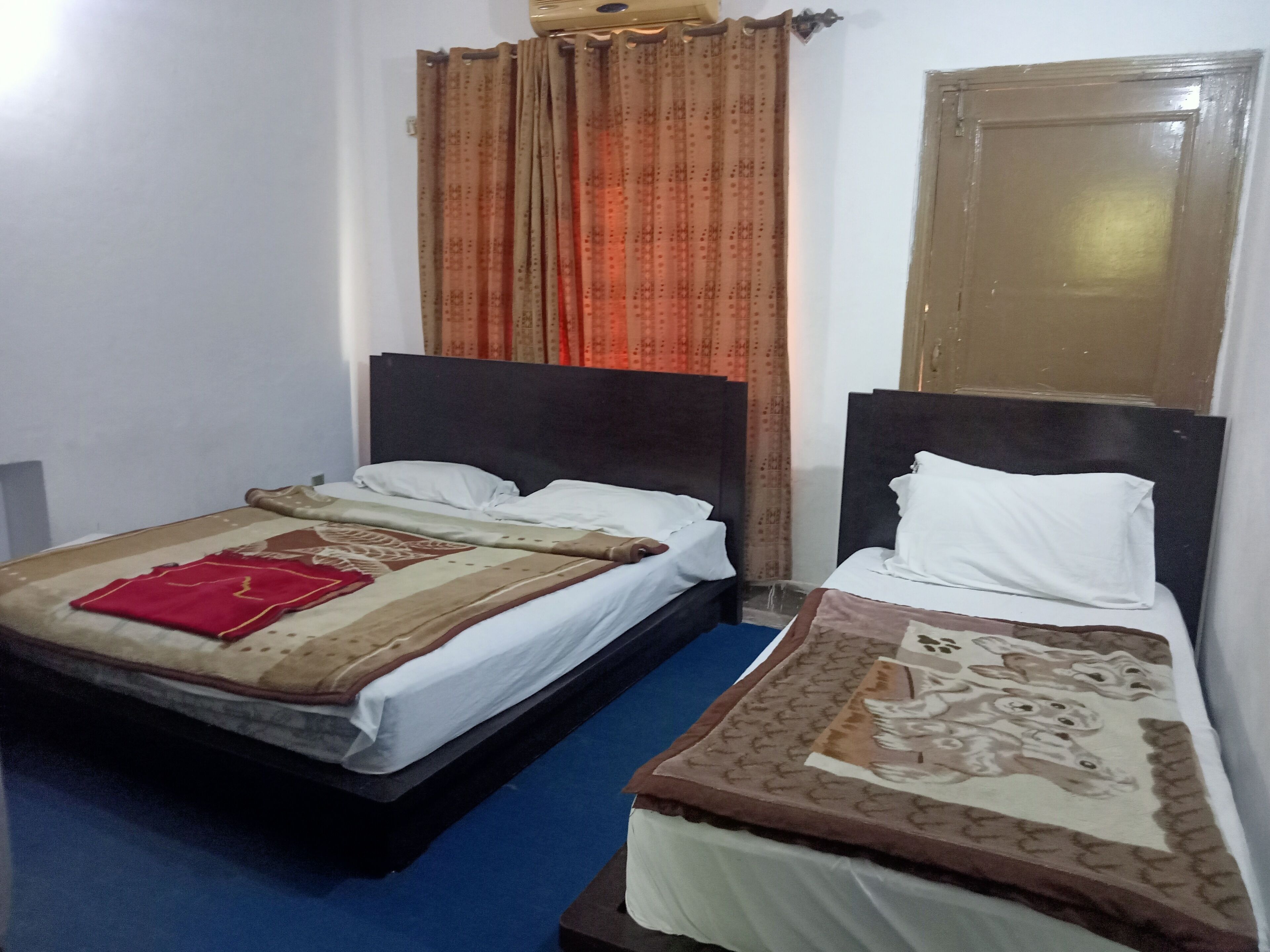 A hotel room with two beds, each with a headboard, a window with curtains, and a door.