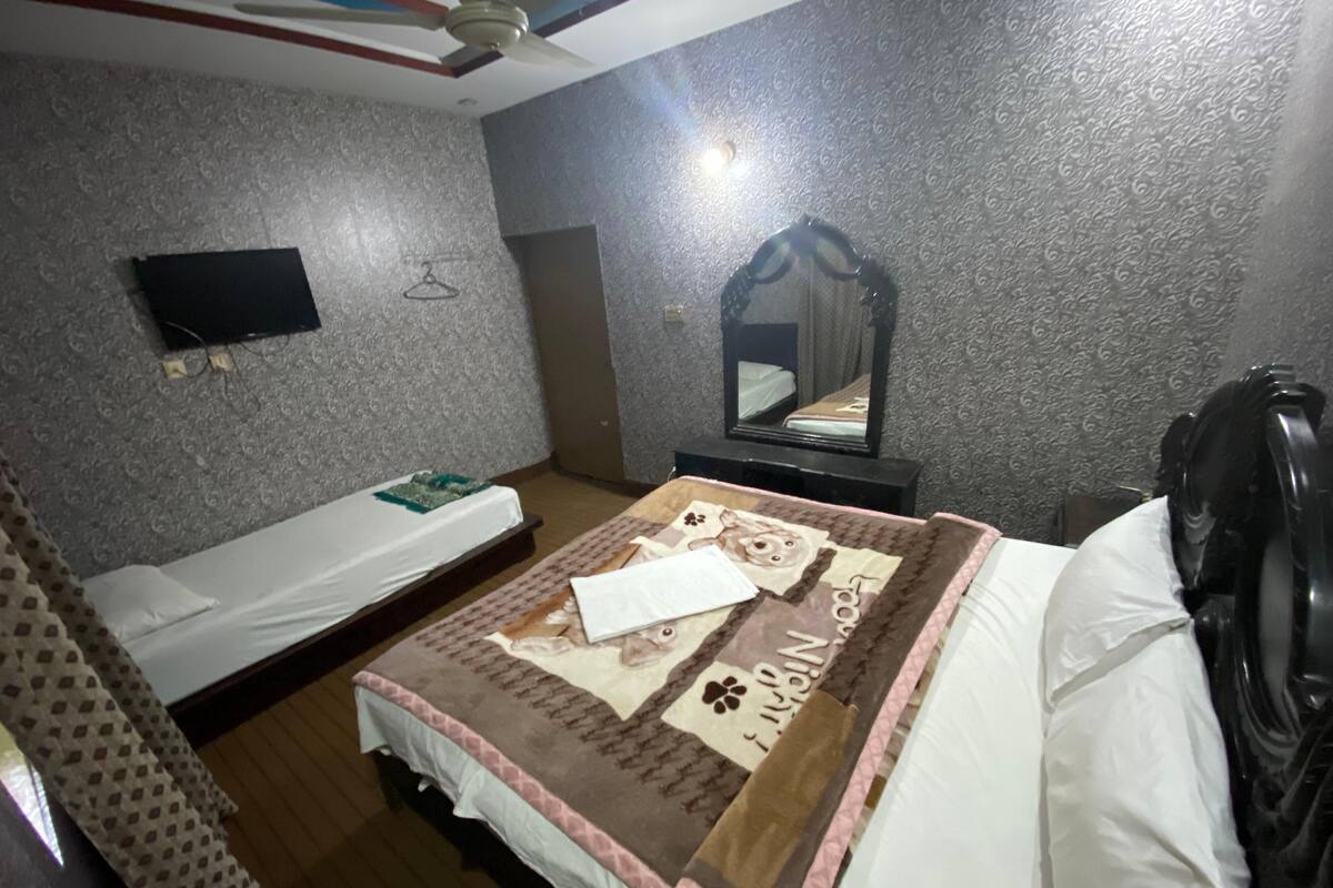 Une chambre avec un lit, une table de chevet, un miroir et un téléviseur fixé au mur.