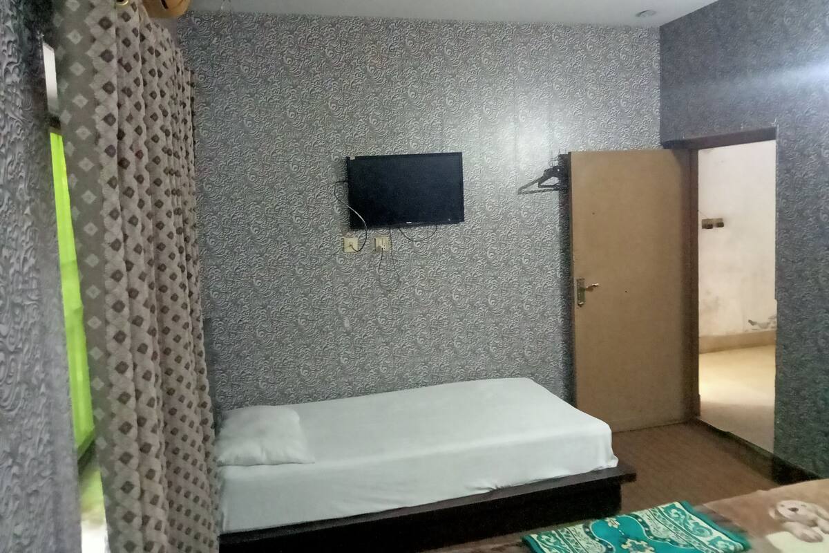 Une pièce avec un lit, un téléviseur fixé au mur et une porte.