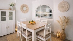 A dining area with a wooden table, white chairs, a fruit basket, a cabinet with glass doors, and decorative wall art. - Bela Vista Apartment (Luz)