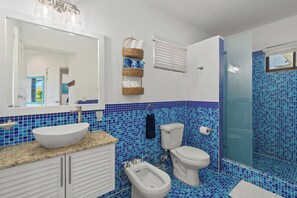 Et badeværelse med en hvid vask, en bidet, et toilet og en brusekabine med glasvægge.