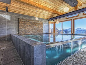 Un moderno espacio de spa con un jacuzzi de paredes de vidrio, paredes de piedra, techo de madera y vistas a las montañas.