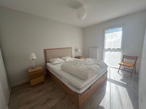Quarto com cama de madeira, mesas de cabeceira, uma cadeira e janela com cortinas.