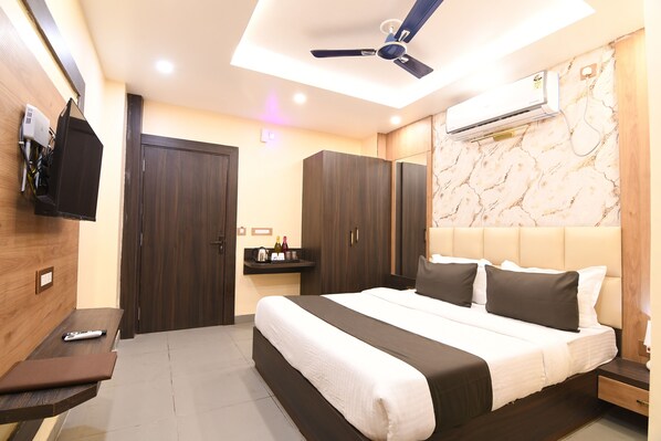 Ein modernes Hotelzimmer mit einem großen Bett, einem Deckenventilator, einer Klimaanlage, einem an der Wand montierten Fernseher und einem kleinen Tisch mit einer Fernbedienung.