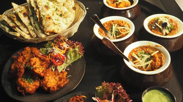 A table with various dishes including naan bread, fried items, and bowls of curry. - NB SONARBANGLA HOTEL & RESTAURANT (Kalyani)