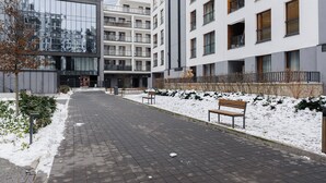 Un sendero urbano cubierto de nieve, con bancos, edificios modernos y fachada de vidrio reflectante.