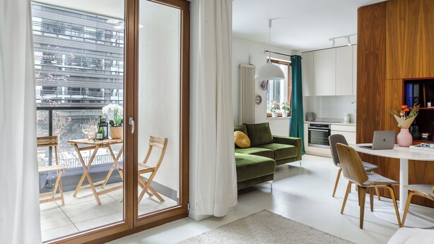 Un apartamento moderno con balcón, un sofá verde, una mesa de comedor y una zona de cocina.