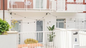 A two-story building with a 'VINO' sign, balconies with white railings, and a small outdoor seating area with a yellow sofa.