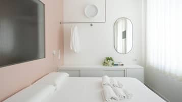 Una camera d'albergo con un letto grande, un comodino con uno specchio, un appendi asciugamani e una finestra con tende.