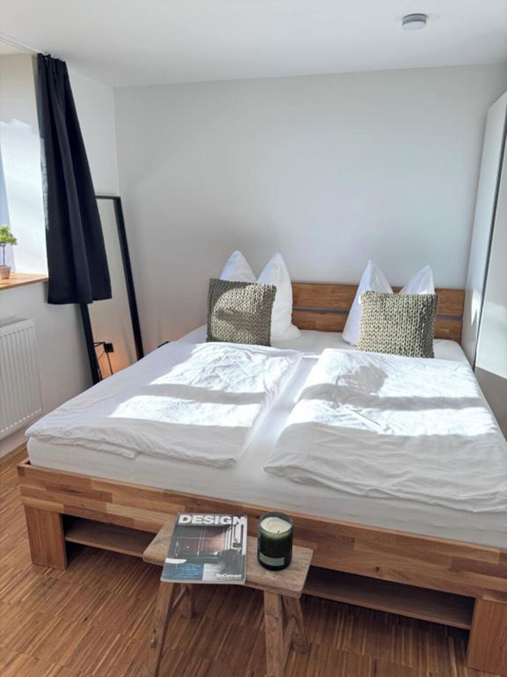 Un lit bien fait, avec du linge de lit blanc, un magazine posé sur la table de chevet et une petite table sur laquelle se trouve une bougie.