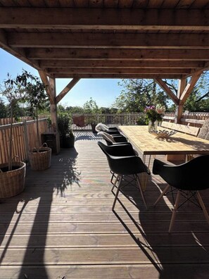 Une terrasse extérieure en bois, avec une table et des chaises, entourée d’une clôture en bois et d’arbres.