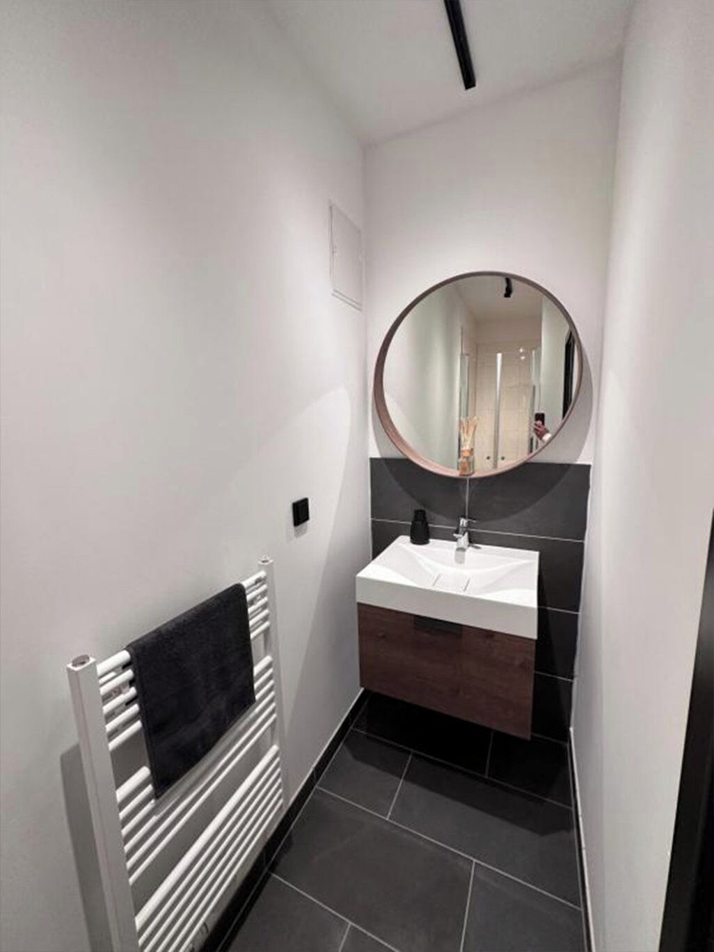 A modern bathroom with a white vanity, a round mirror, and a towel rack.