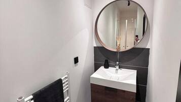 A modern bathroom with a white vanity, a round mirror, and a towel rack.
