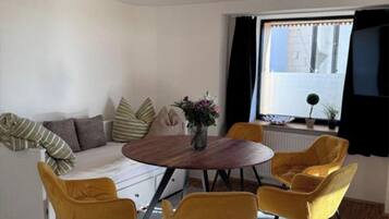 A modern living room with a sofa, a round wooden table, and four yellow chairs.