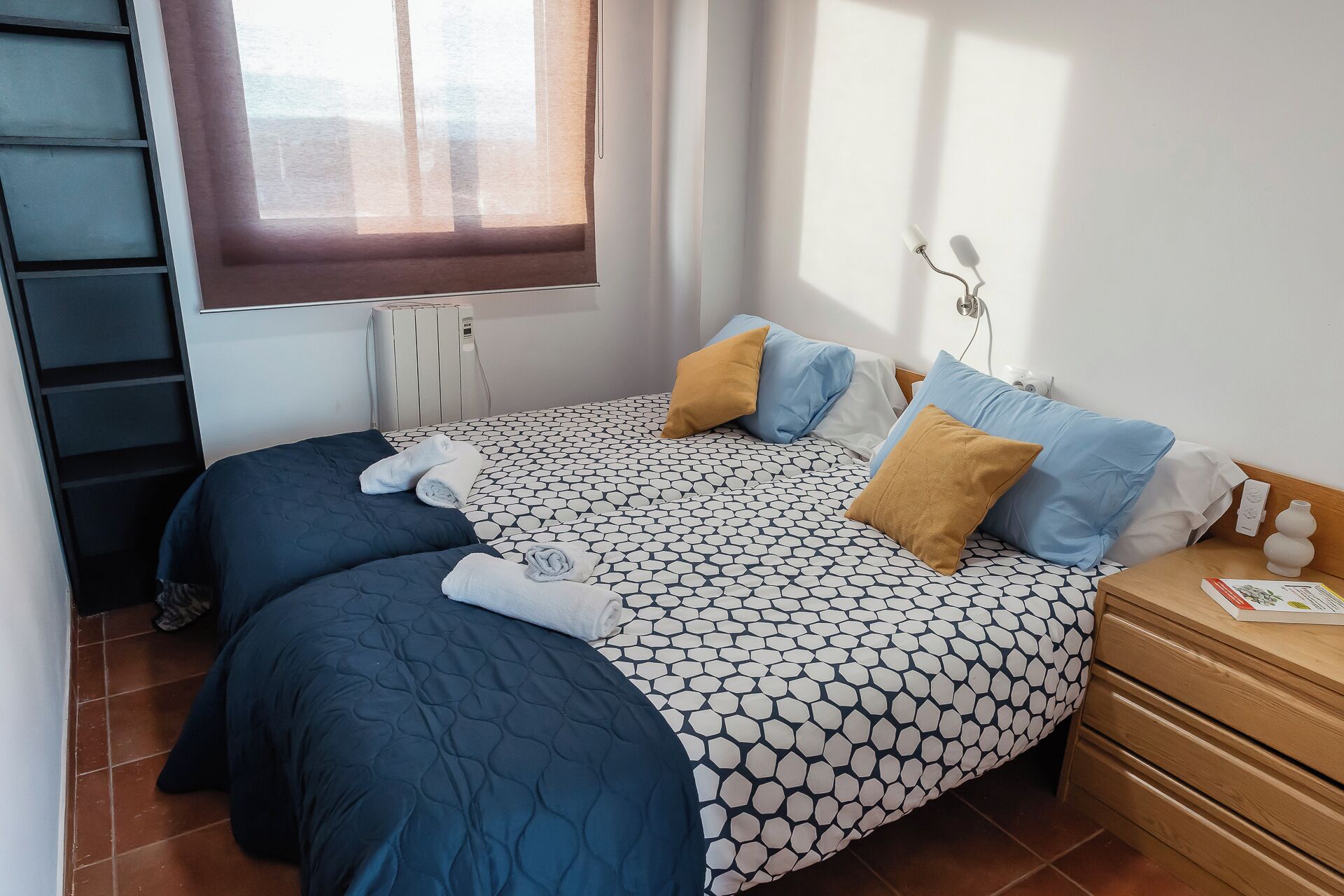 Un llit ben arropat amb un estovat estampat, dues almoines i tovalloles esteses.