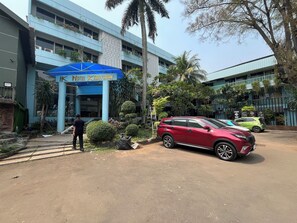 A hotel entrance with a blue canopy, palm trees, and a red car parked in front. - Hotel O Kebayoran (Jakarta)