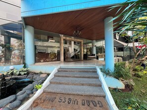 A modern building entrance with a covered porch, a stone staircase leading to the entrance, and a small water feature with rocks. - Hotel O Kebayoran (Jakarta)