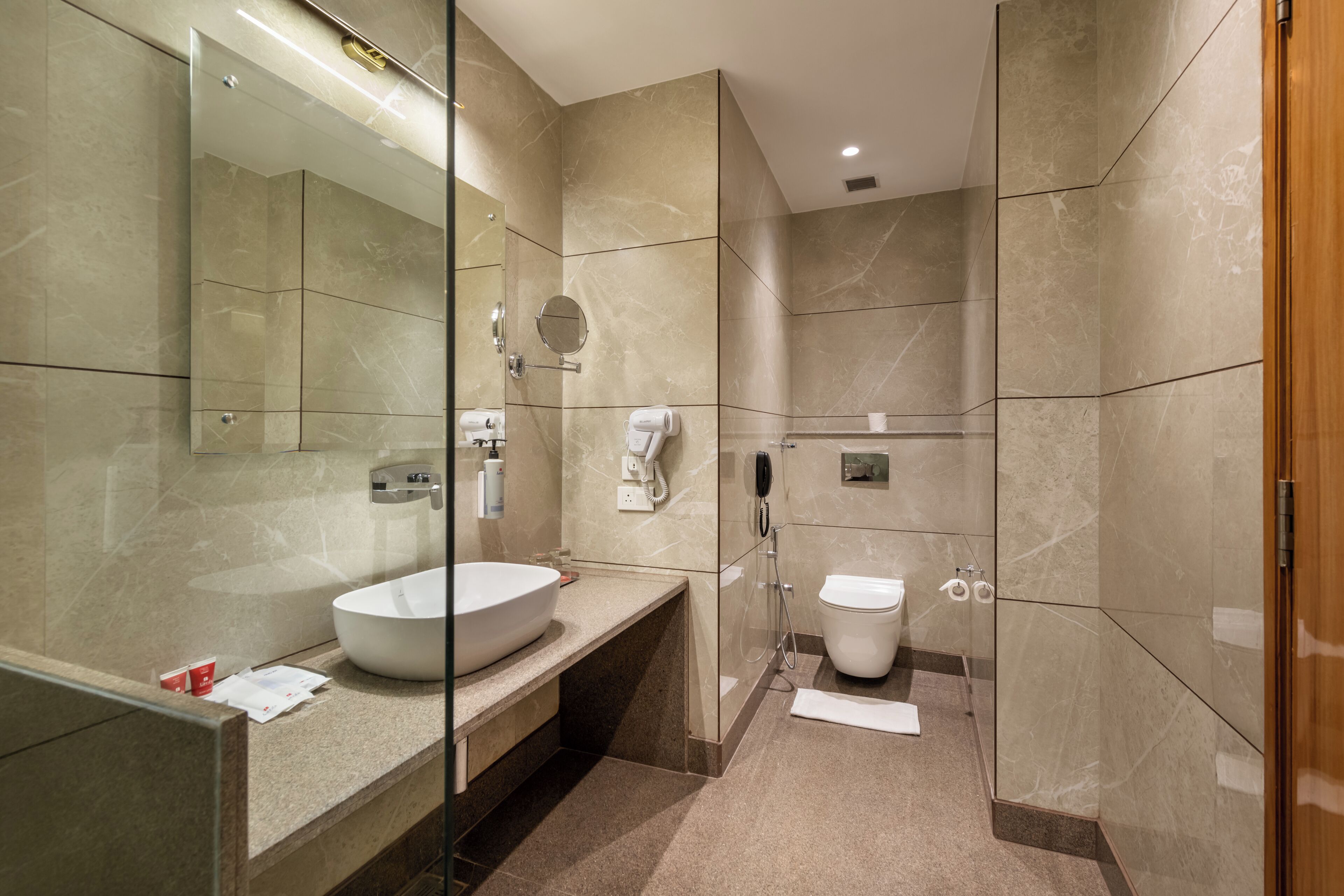 A modern bathroom with a large mirror, a round sink, and a toilet.