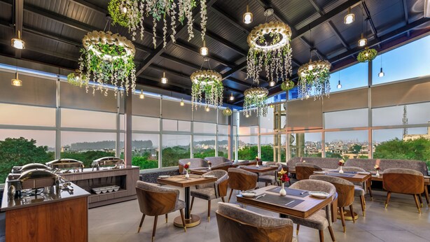 Un ristorante moderno con ampie finestre, arredi in legno e decorazioni floreali pendenti.