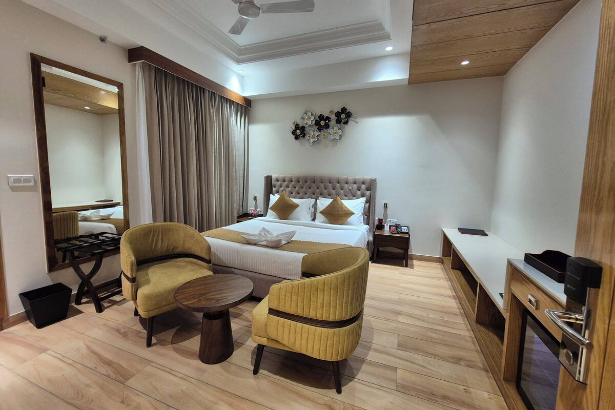 A hotel room with a bed, two armchairs, a small table, a desk, and a mirror.