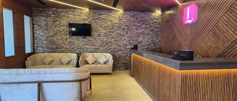 A modern reception area with a stone wall, two sofas, a wooden reception desk, and a neon sign.