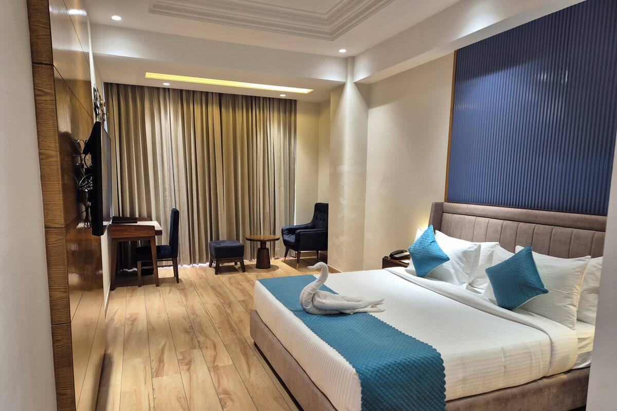 A hotel room with a large bed, a desk, a chair, and a television.