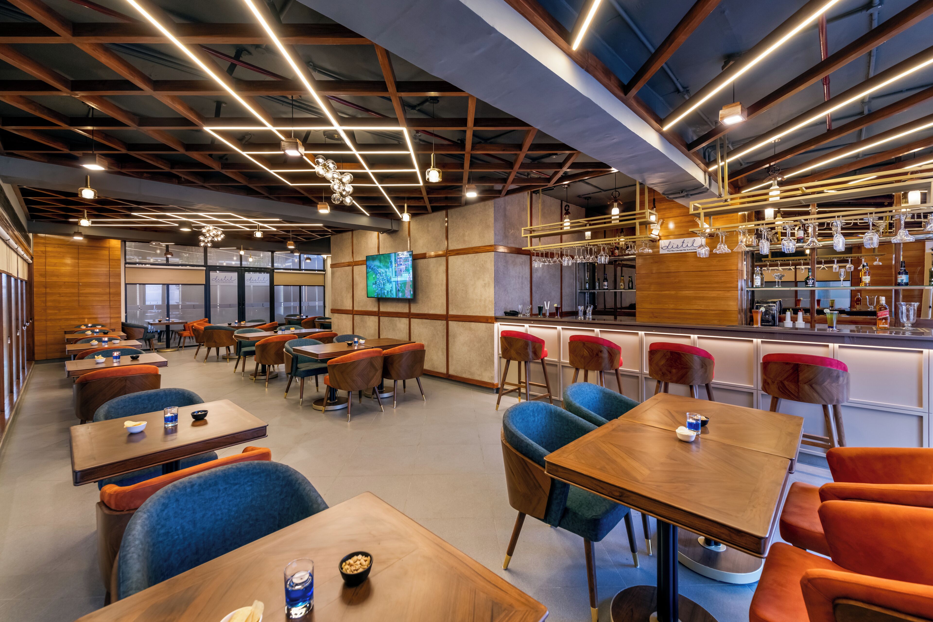 Un restaurante moderno con varias zonas de estar, una barra y una pantalla de televisión.
