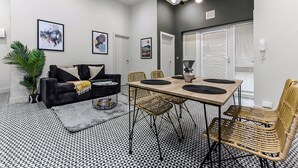 A modern living room with a black and white patterned floor, a black sofa with cushions, a dining table with chairs, and framed artwork on the walls. - Convenient 2BR 2BA / near Tube Station (London)