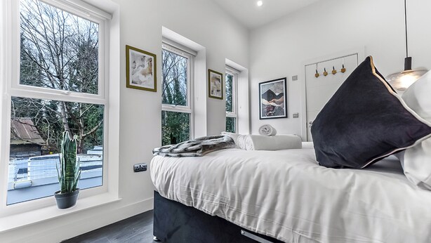 A modern bedroom with a bed, bedside tables, a potted plant, and large windows. - Convenient 2BR 2BA / near Tube Station (London)
